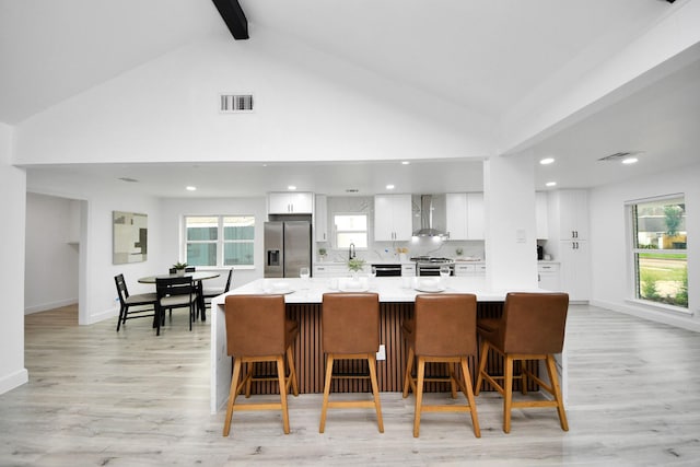 kitchen featuring a kitchen breakfast bar, a large island, stainless steel appliances, wall chimney exhaust hood, and white cabinets