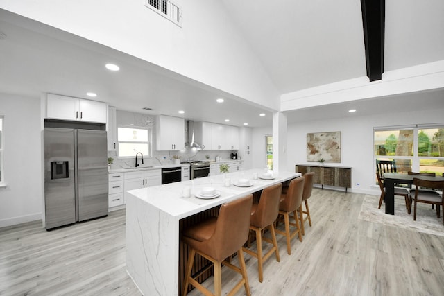 kitchen with appliances with stainless steel finishes, white cabinets, a center island, and wall chimney exhaust hood