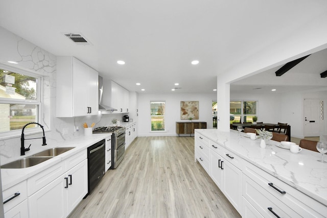 kitchen with black dishwasher, sink, range with two ovens, white cabinets, and wall chimney range hood