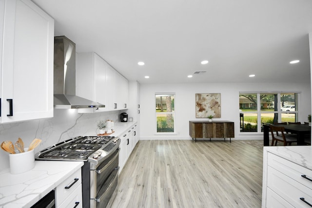 kitchen featuring double oven range, white cabinets, light stone countertops, and wall chimney exhaust hood