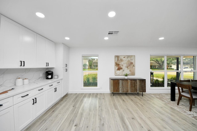 kitchen featuring light hardwood / wood-style flooring, light stone countertops, white cabinets, and backsplash