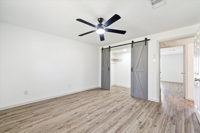 unfurnished bedroom featuring light wood-type flooring, ceiling fan, and a barn door