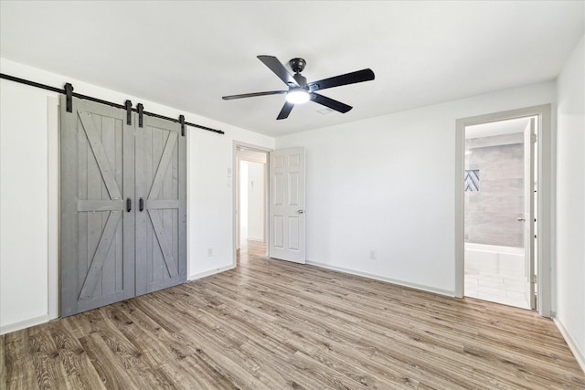 unfurnished bedroom with ceiling fan, light hardwood / wood-style flooring, ensuite bath, and a barn door