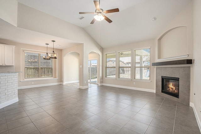 unfurnished living room with a fireplace, tile patterned floors, vaulted ceiling, baseboards, and ceiling fan with notable chandelier