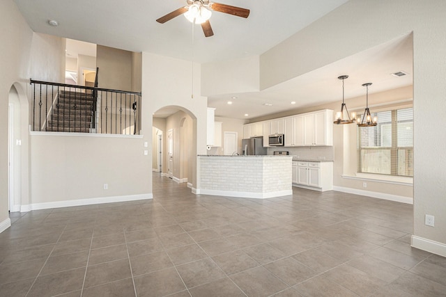 unfurnished living room featuring baseboards, arched walkways, dark tile patterned flooring, ceiling fan with notable chandelier, and recessed lighting