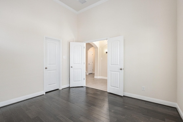 unfurnished room featuring dark wood-type flooring, arched walkways, crown molding, and baseboards