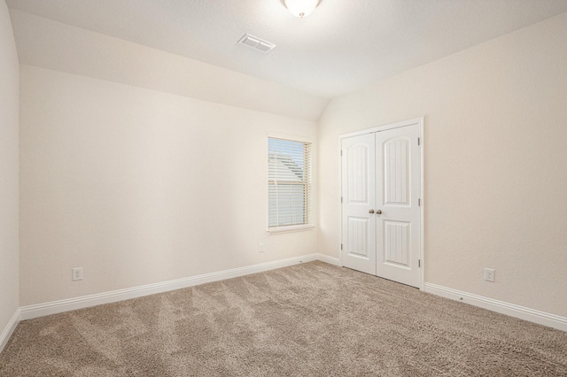 carpeted empty room with vaulted ceiling, visible vents, and baseboards