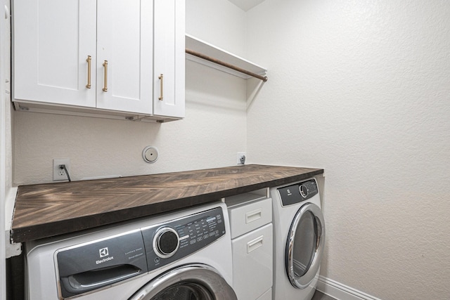 laundry room featuring baseboards, cabinet space, a textured wall, and washing machine and clothes dryer