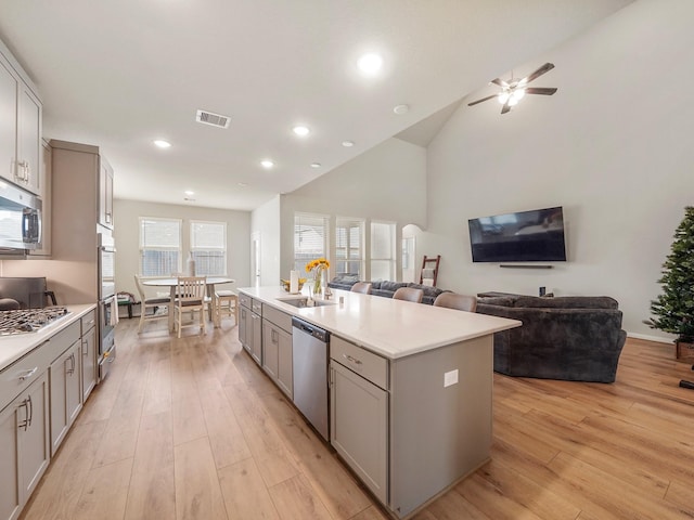 kitchen featuring light wood-type flooring, an island with sink, gray cabinetry, sink, and appliances with stainless steel finishes