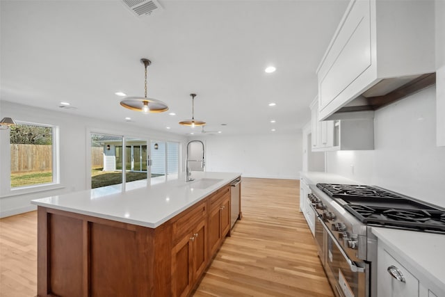 kitchen featuring light wood finished floors, appliances with stainless steel finishes, light countertops, pendant lighting, and a sink