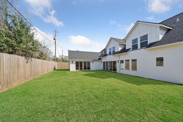 back of house featuring a fenced backyard, a shingled roof, board and batten siding, and a yard