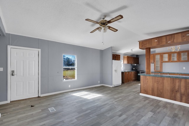 kitchen featuring white refrigerator with ice dispenser, wood finished floors, a ceiling fan, brown cabinets, and dark countertops