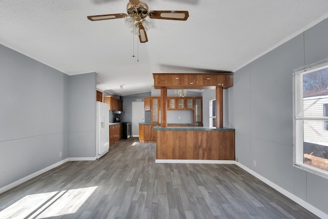 kitchen featuring white refrigerator with ice dispenser, vaulted ceiling, brown cabinetry, dark countertops, and glass insert cabinets