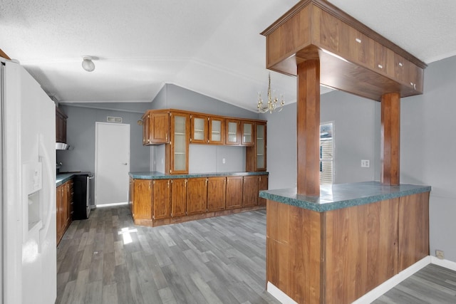 kitchen with dark countertops, a peninsula, glass insert cabinets, and brown cabinetry