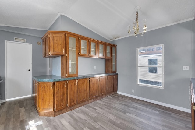 kitchen featuring dark countertops, glass insert cabinets, brown cabinets, vaulted ceiling, and crown molding