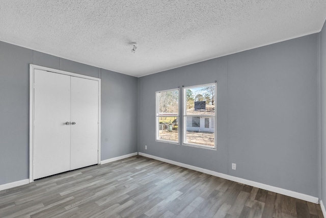 unfurnished bedroom featuring a textured ceiling, a closet, light wood-style flooring, and baseboards