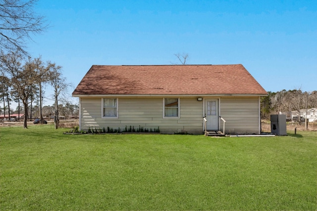 back of house with a shingled roof, entry steps, and a lawn