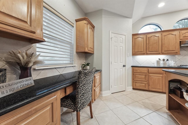 kitchen featuring backsplash, dark stone countertops, built in desk, and light tile patterned floors