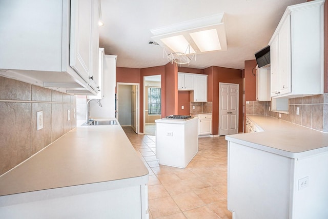 kitchen with a center island, a sink, light countertops, white cabinetry, and backsplash