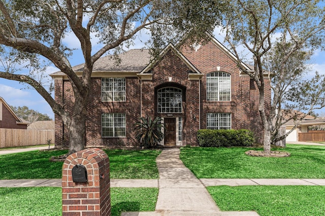 traditional home featuring a front yard, brick siding, and fence