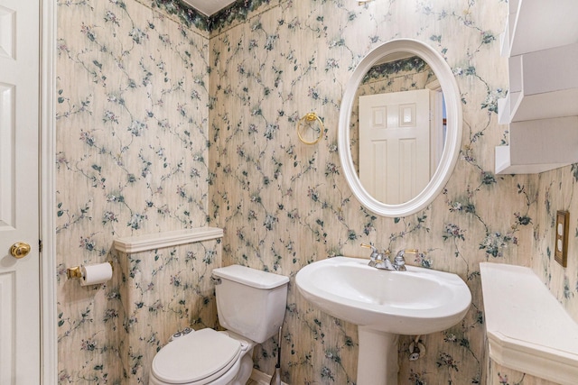 half bath with toilet, wallpapered walls, and a sink