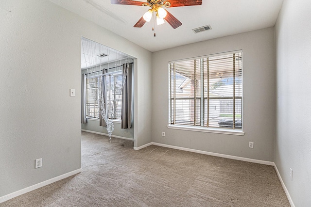 spare room with baseboards, visible vents, a ceiling fan, and light colored carpet