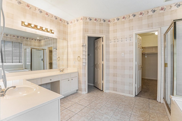 full bathroom with a walk in closet, wallpapered walls, a shower stall, vanity, and tile patterned floors