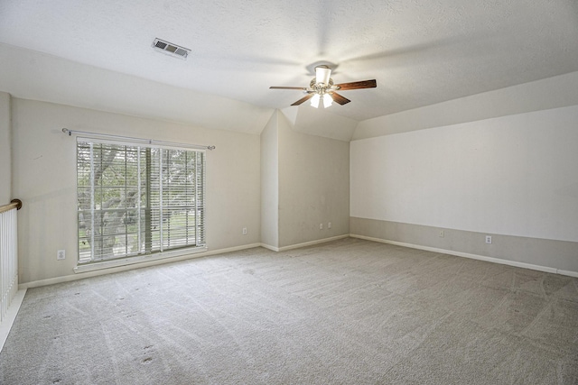 unfurnished room with visible vents, vaulted ceiling, a textured ceiling, and light colored carpet