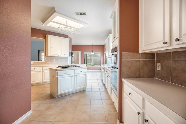 kitchen featuring light tile patterned floors, tasteful backsplash, light countertops, hanging light fixtures, and visible vents