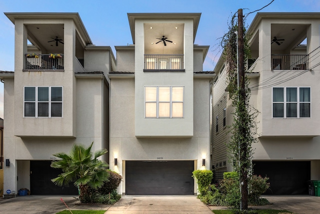 view of front of home with a garage, a ceiling fan, stucco siding, and a balcony