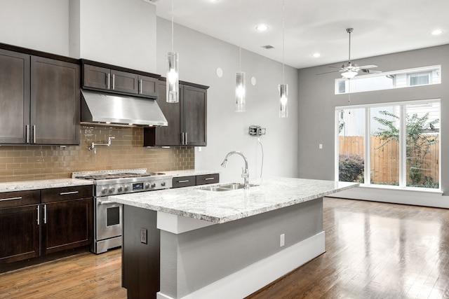 kitchen with high end stove, under cabinet range hood, light stone counters, light wood-style flooring, and a sink