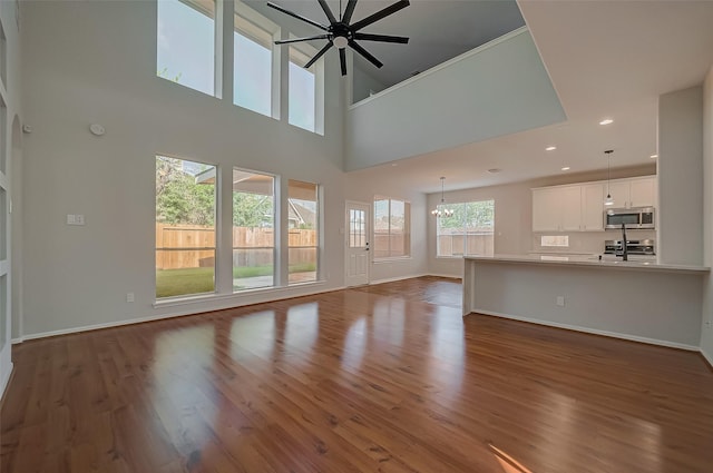 unfurnished living room with ceiling fan with notable chandelier, dark wood-type flooring, and a towering ceiling