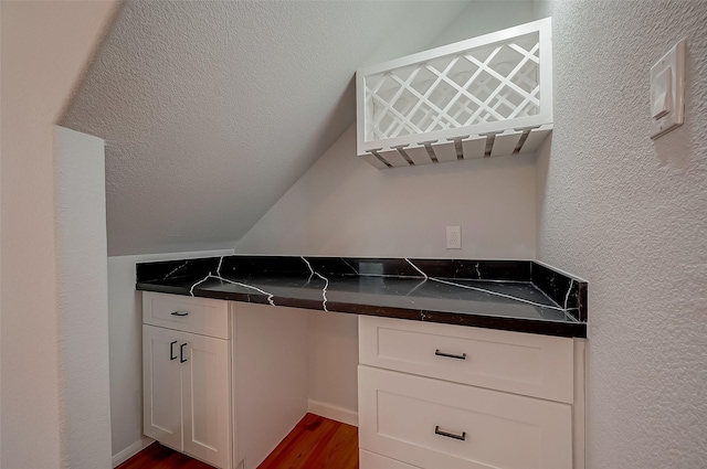 kitchen featuring built in desk, dark wood-type flooring, a textured ceiling, lofted ceiling, and white cabinetry