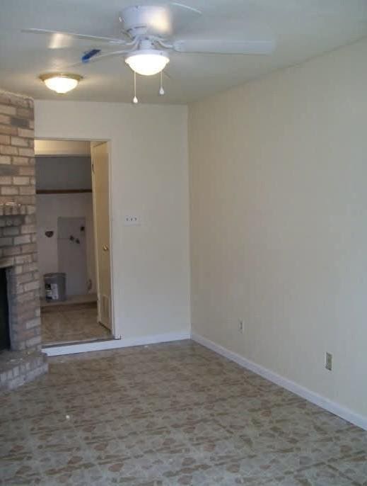 empty room with a fireplace and ceiling fan