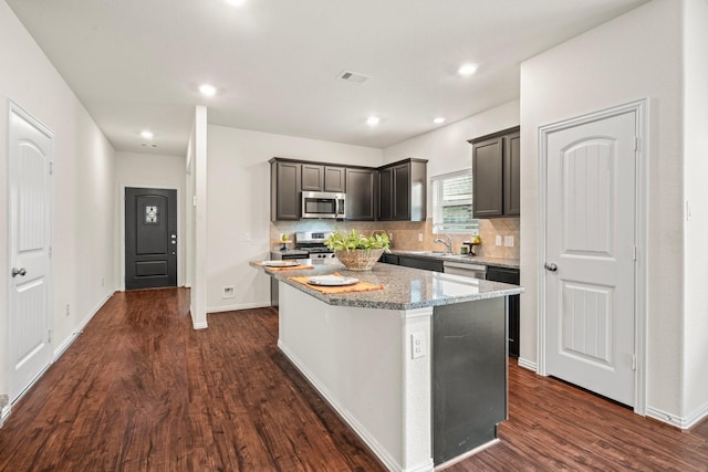 kitchen with a kitchen island, light stone counters, stainless steel appliances, and backsplash