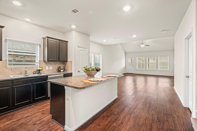 kitchen with light stone counters, a sink, visible vents, open floor plan, and a center island