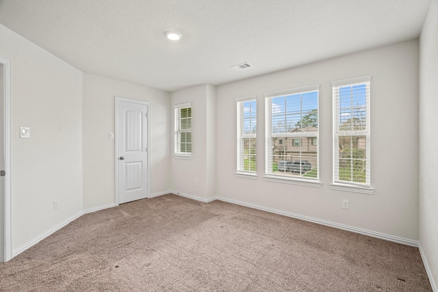 empty room featuring light colored carpet, visible vents, and baseboards