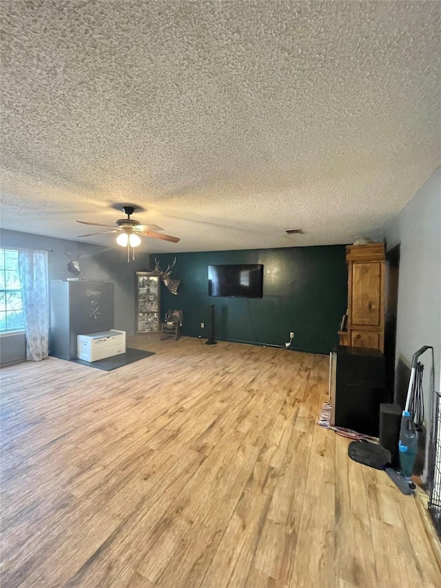 living room with light wood-type flooring, a wood stove, a textured ceiling, and ceiling fan