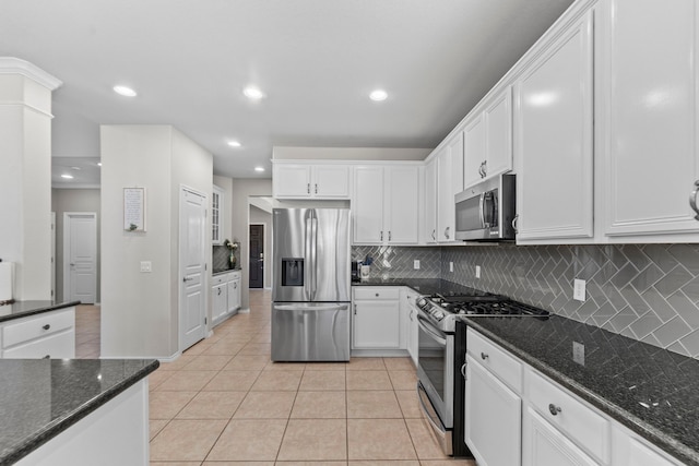 kitchen with stainless steel appliances, backsplash, light tile patterned floors, dark stone counters, and white cabinets