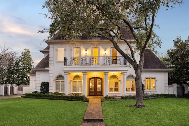 view of front of home with french doors, a lawn, a balcony, and stucco siding