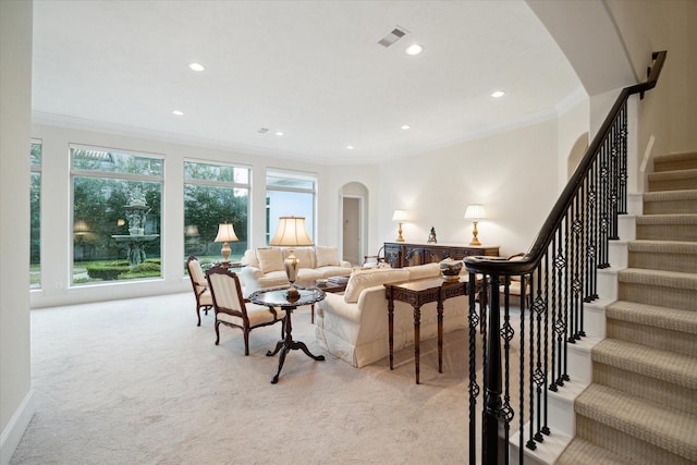 living area with light carpet, visible vents, arched walkways, and ornamental molding