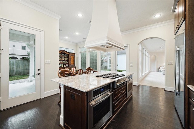 kitchen featuring a breakfast bar area, appliances with stainless steel finishes, a center island, dark brown cabinets, and premium range hood