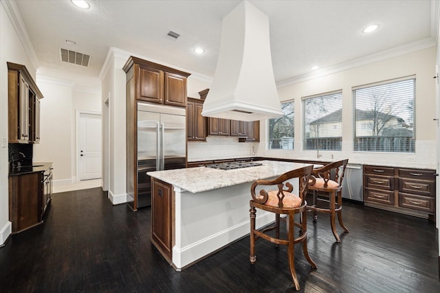 kitchen featuring light stone counters, premium range hood, a kitchen island, visible vents, and appliances with stainless steel finishes