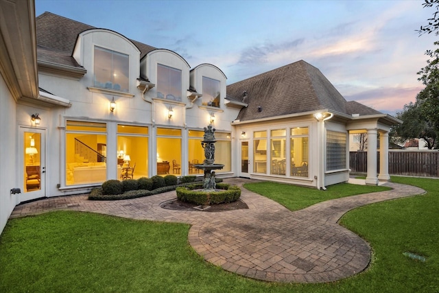 back of property featuring a shingled roof, fence, a lawn, and a patio