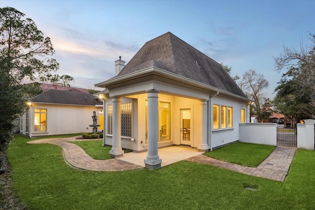 back of property at dusk featuring a shingled roof, a chimney, a gate, fence, and a yard