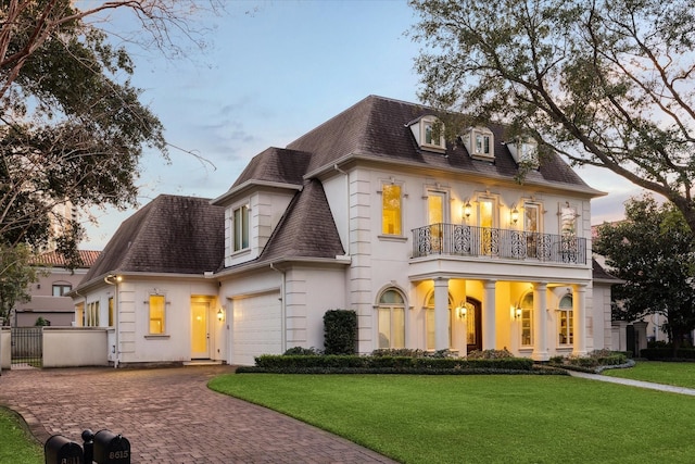 view of front of house with decorative driveway, a shingled roof, fence, a balcony, and a front lawn