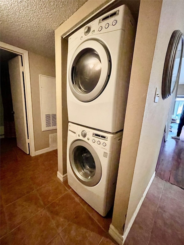 clothes washing area with dark tile patterned flooring, a textured ceiling, and stacked washer / drying machine