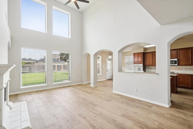 unfurnished living room with a towering ceiling, light wood-style floors, baseboards, and a ceiling fan