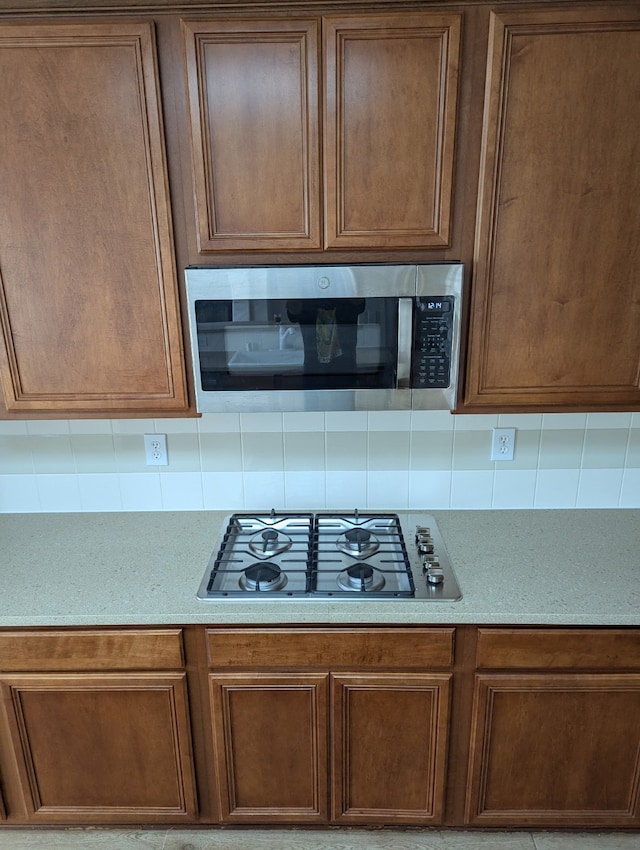 kitchen featuring stainless steel microwave, gas cooktop, brown cabinetry, and decorative backsplash