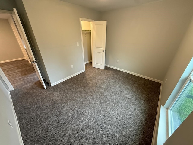 unfurnished bedroom featuring a spacious closet and dark colored carpet